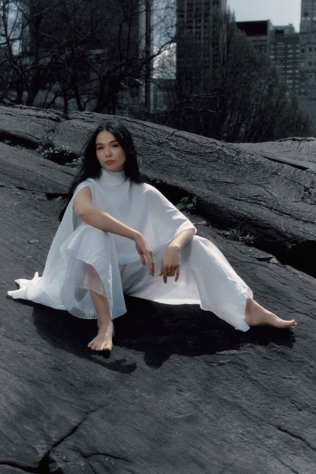 Woman wearing a white silk blouse and trousers with transparent details sitting on a dark textured surface