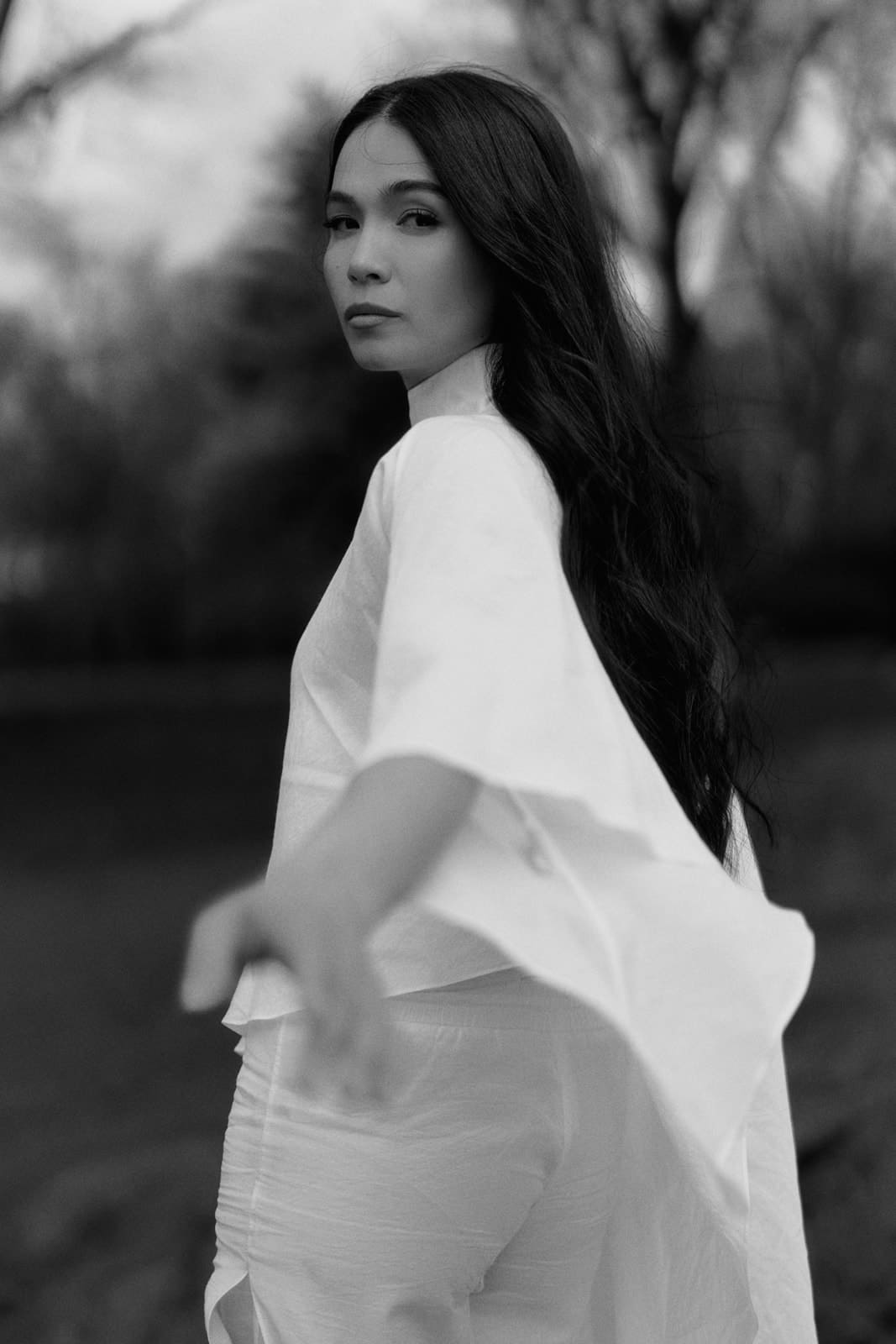 Woman wearing a white silk blouse and trousers with transparent details sitting on a dark textured surface