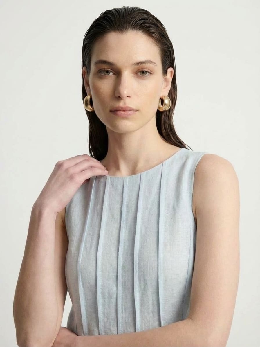 Woman wearing a light blue sleeveless dress against a plain background