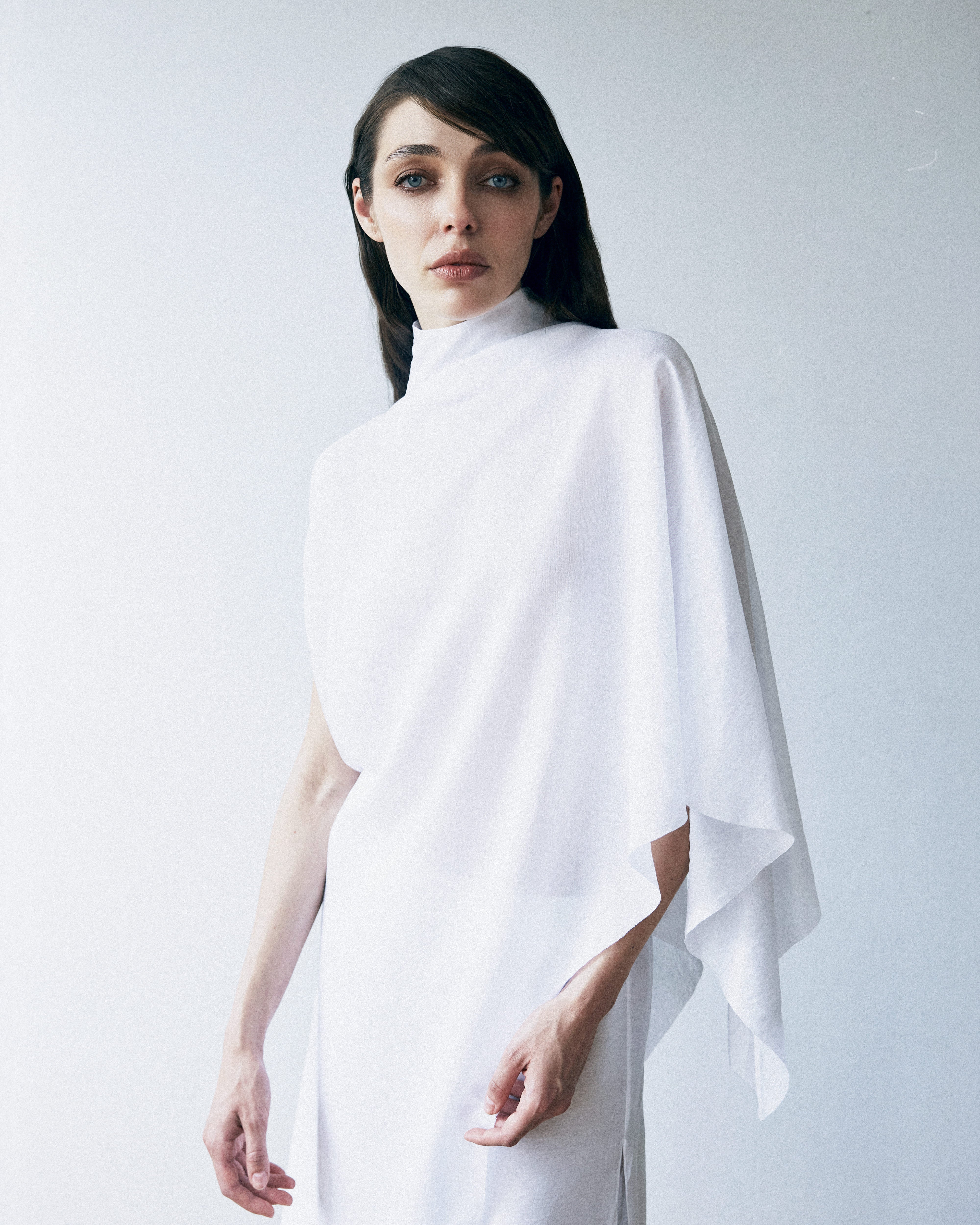 Woman wearing a white poncho against a plain background