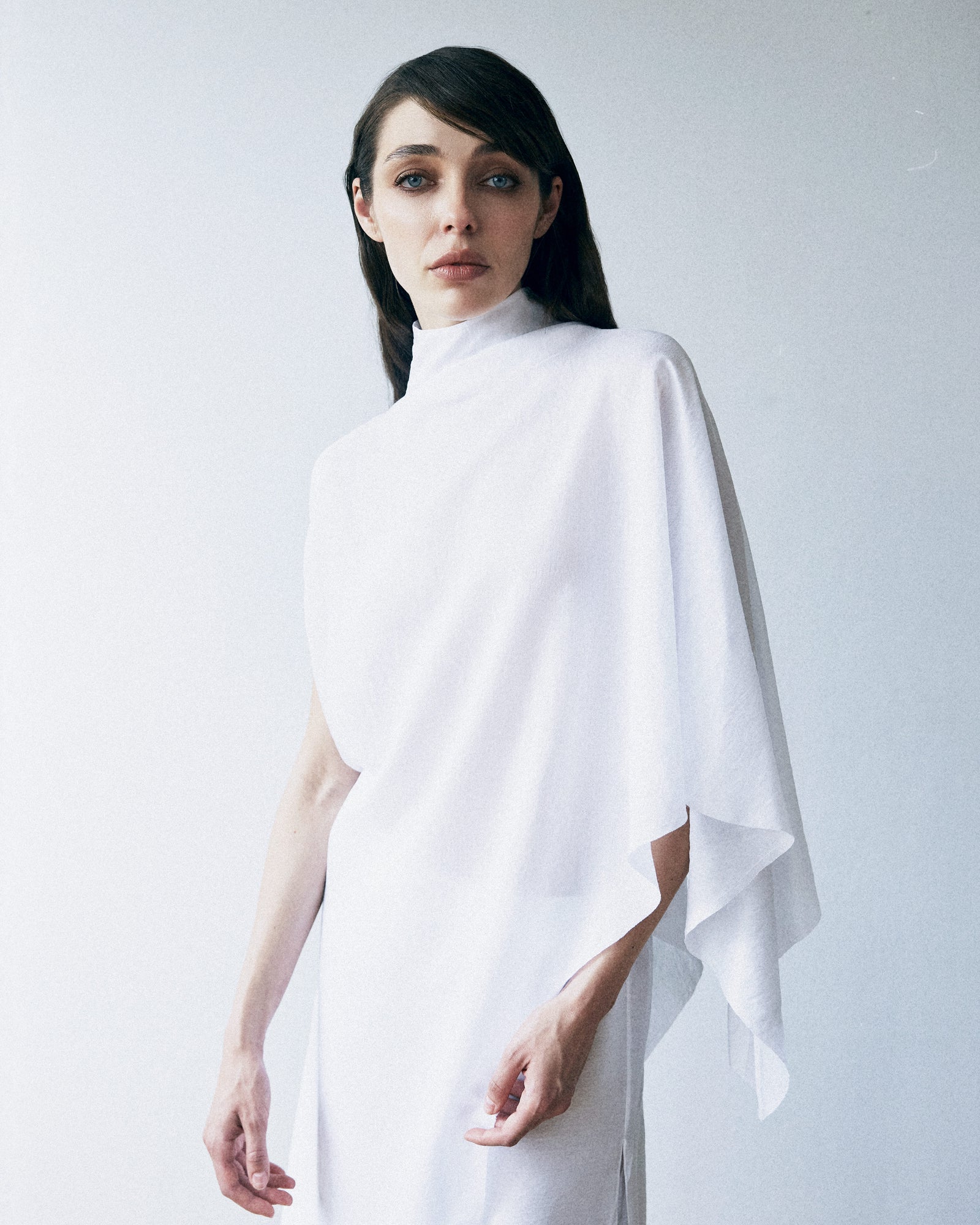Woman wearing a white poncho against a plain background