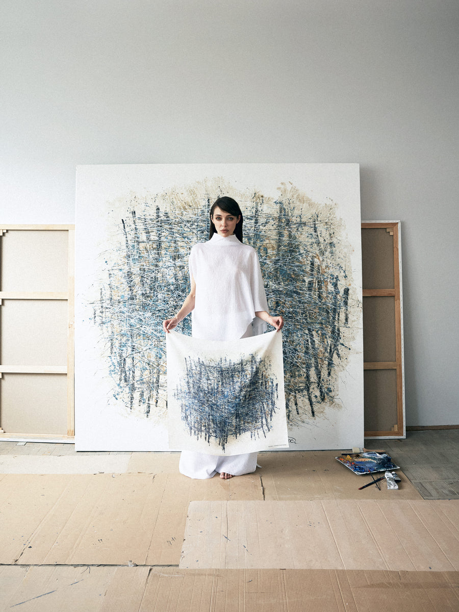 Woman holding a white fabric in front of a large abstract painting in a minimalistic room.