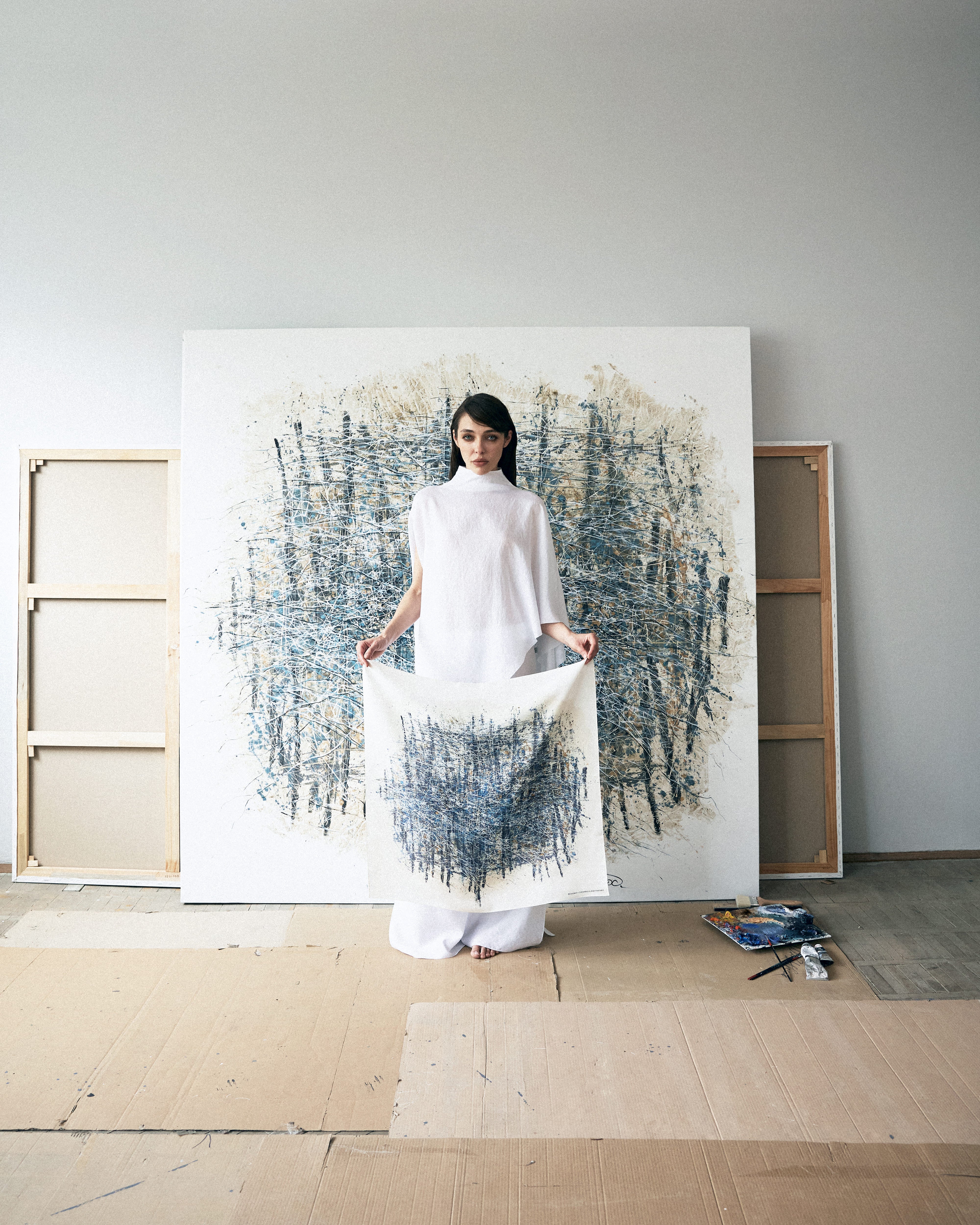 Woman holding a white fabric in front of a large abstract painting in a minimalistic room.