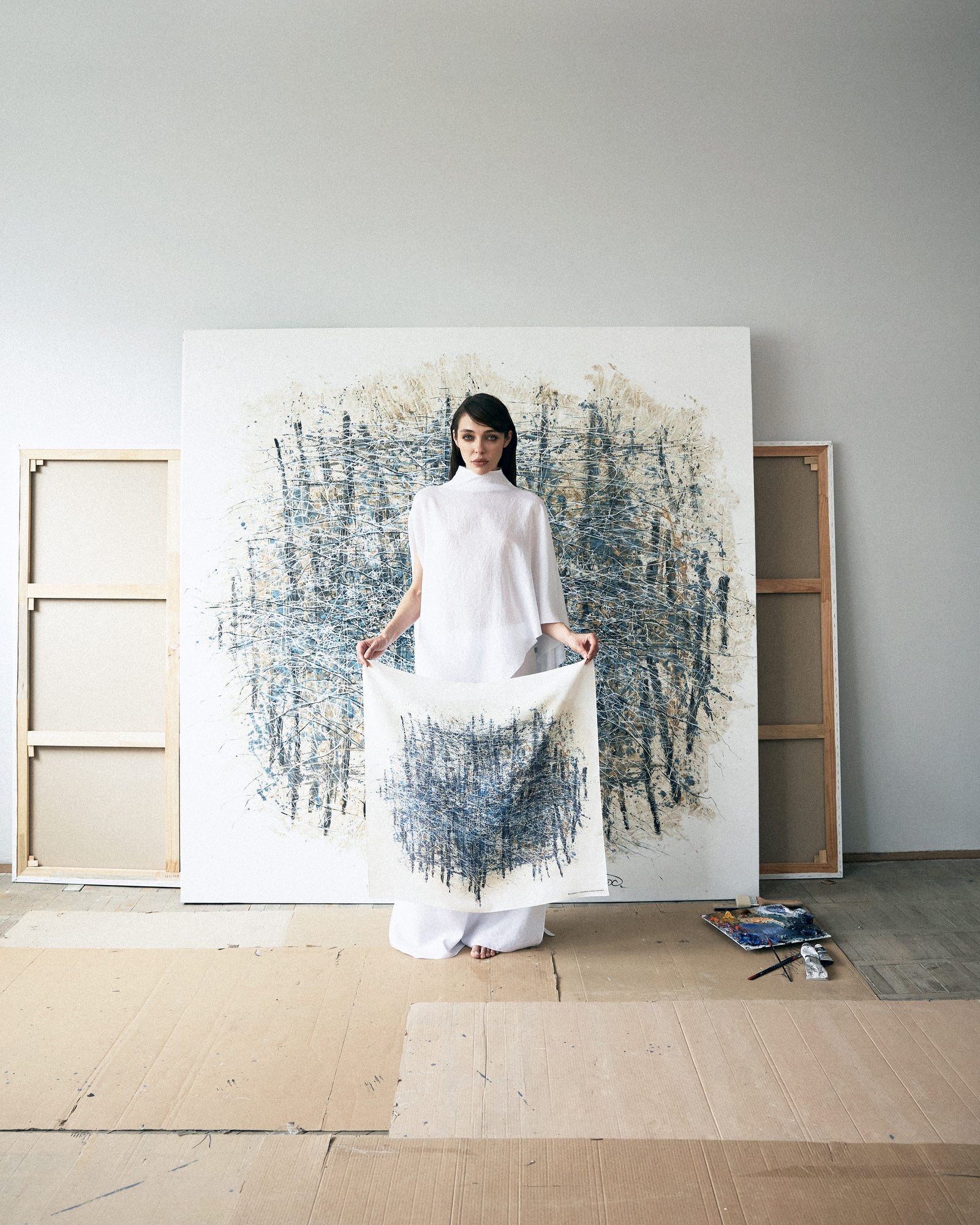 Woman holding a white fabric in front of a large abstract painting in a minimalistic room.