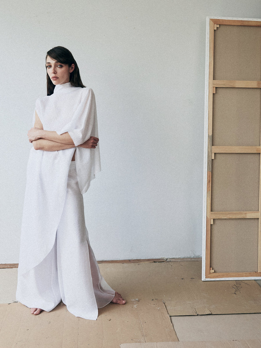 Woman in a white outfit standing in a room with large wooden panels.